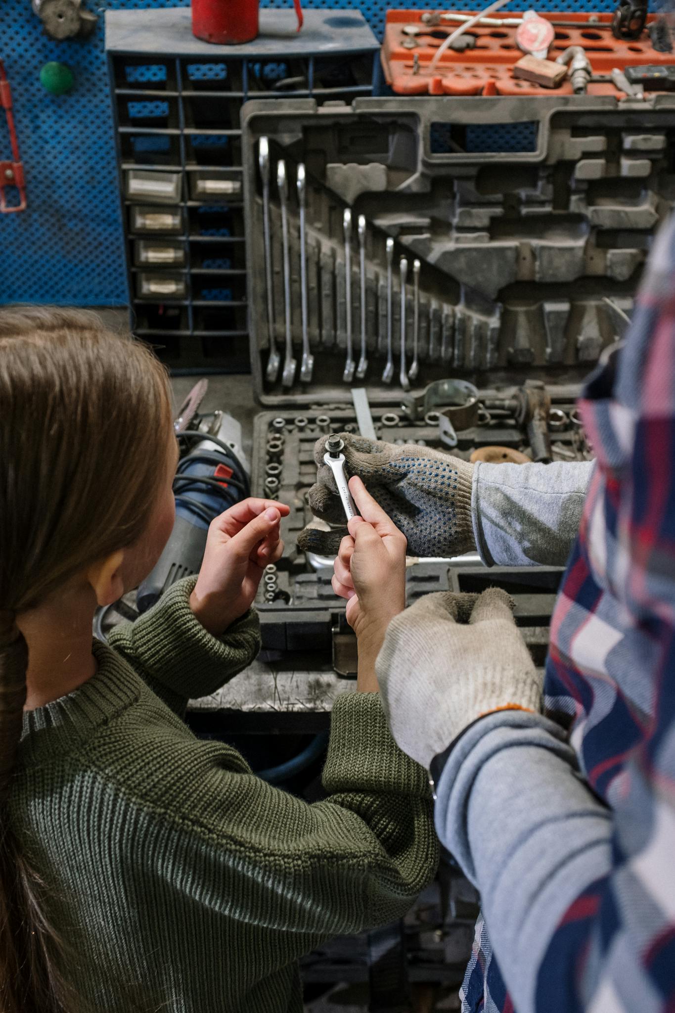 A parent and child collaborate in a garage, learning car repair skills with various tools.