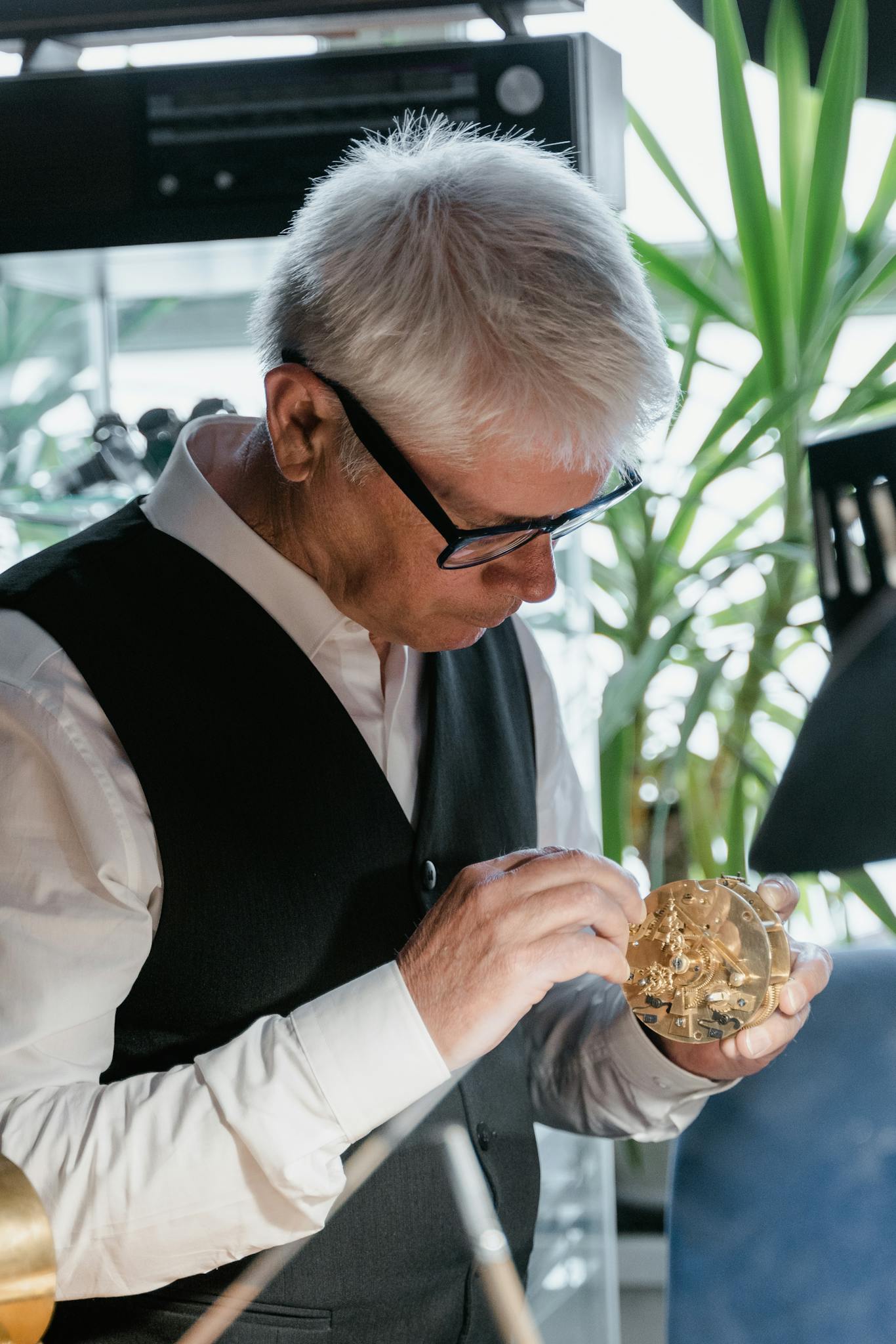 Elderly man carefully examining a clock mechanism in his workshop.
